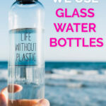 A hand holding a glass water bottle at the beach with the words "Why we use glass water bottles" next to it
