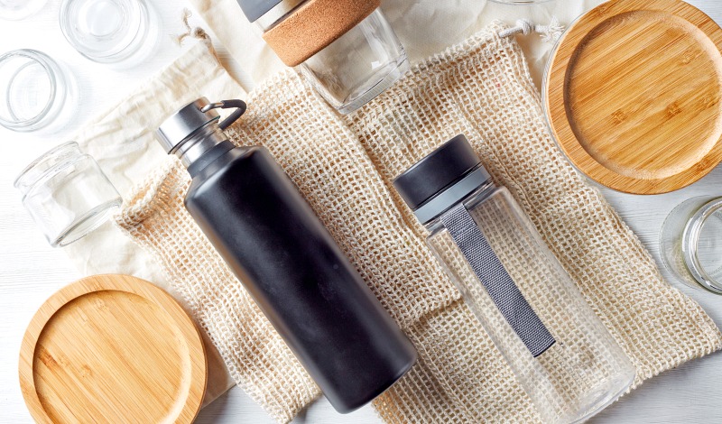 Glass and stainless steel water bottles with other eco-friendly items on a table