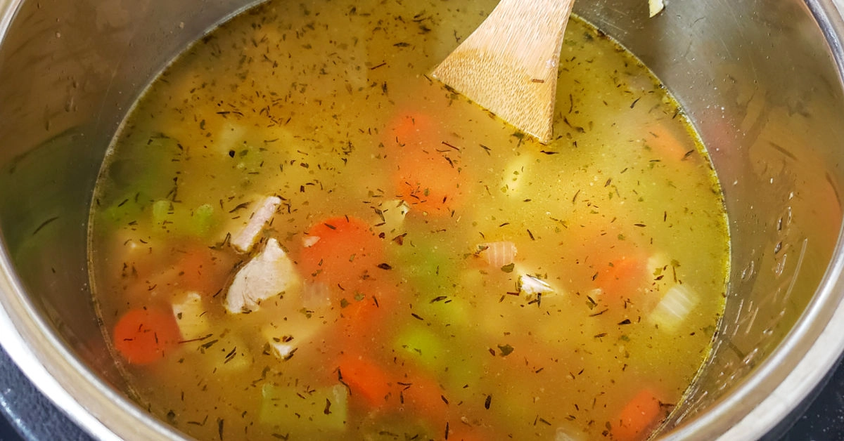 Chicken stock, cooked chicken and spices stirred into vegetables in Instant Pot.