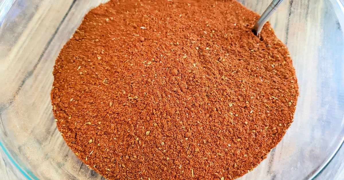 Paprika seasoning being mixed with a fork in a glass mixing bowl.