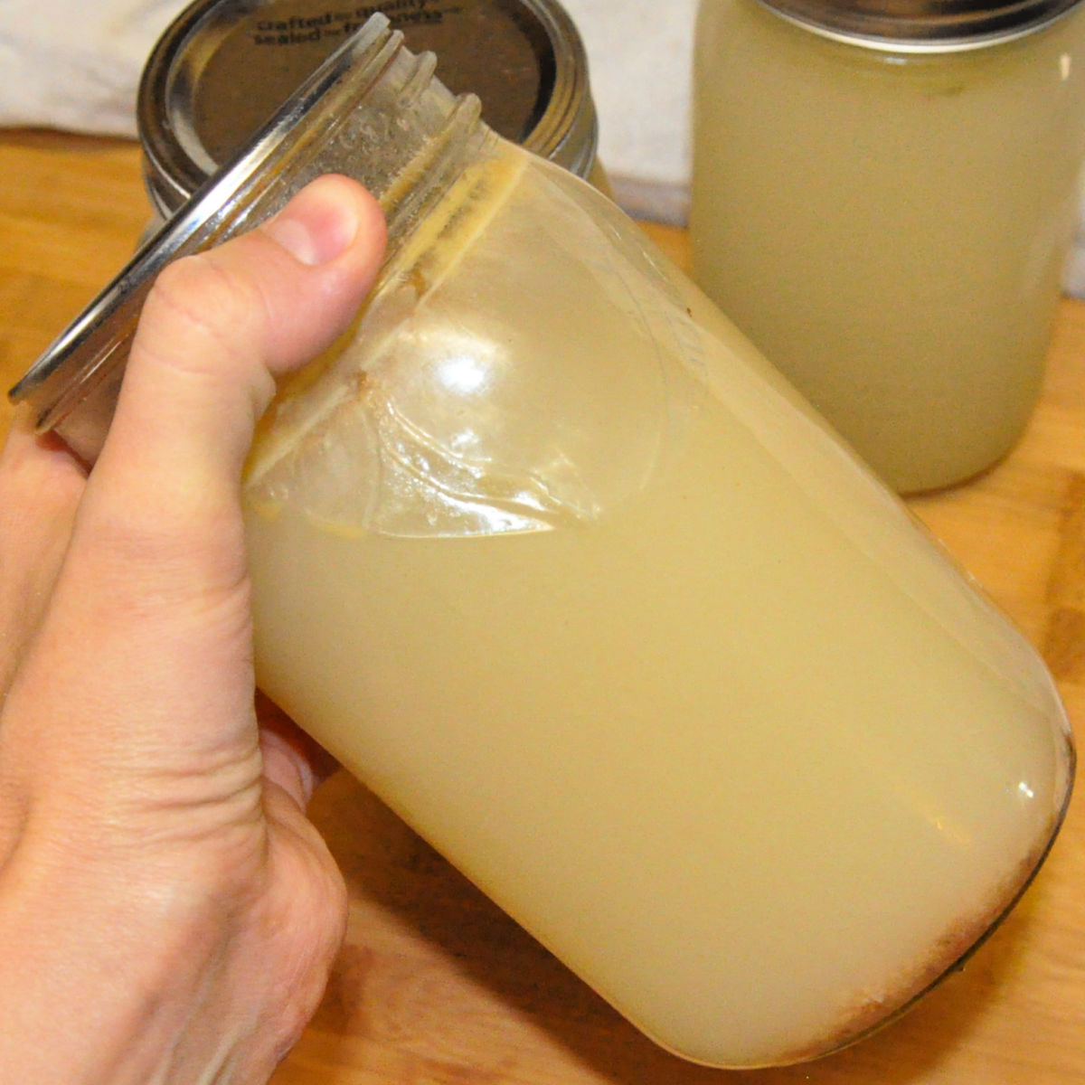 Jar of homemade chicken stock being tilted to show how thick it is.