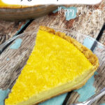 Slice of buttermilk pie with fork on clear glass dessert plate on wood table with worn blue paint.