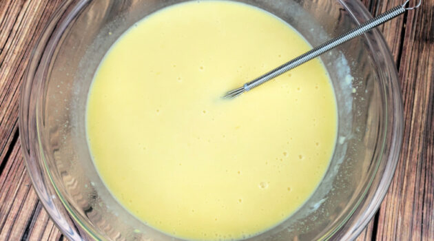 Buttermilk pie filling being whisked in clear glass mixing bowl.