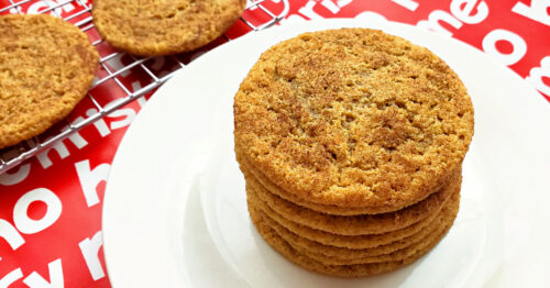 Close up of a stack of homemade gluten free snickerdoodle cookies on a white dessert plate next to a cooling rack.