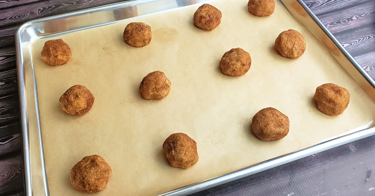 Snickerdoodle cookie dough balls laid out in a parchment paper lined baking sheet.
