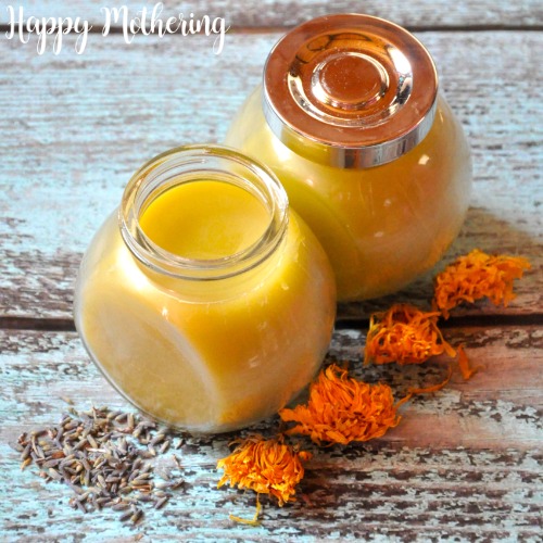 Close up of glass jars of calendula lavender salve on weathered blue wood table with dried flowers