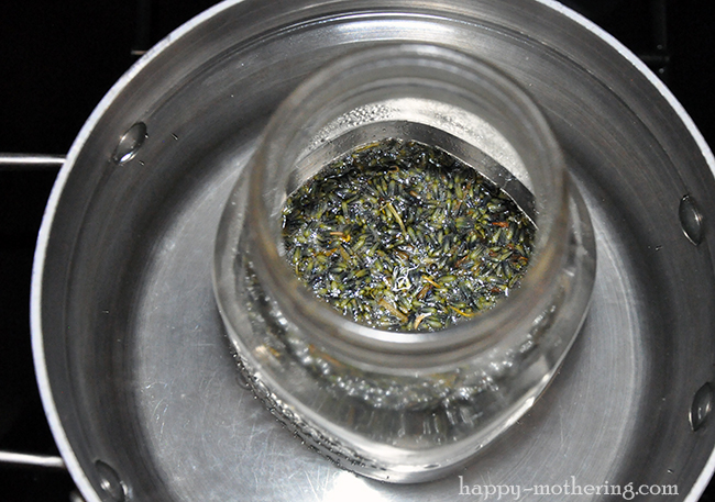 Jar of coconut oil, olive oil, dried lavender and dried calendula in a pan of shallow water