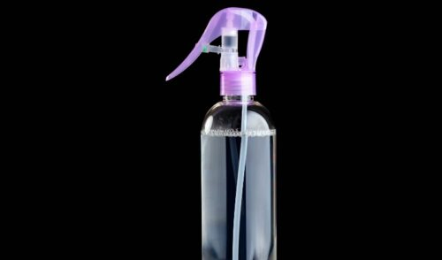 Top half of clear spray bottle with purple top on black background