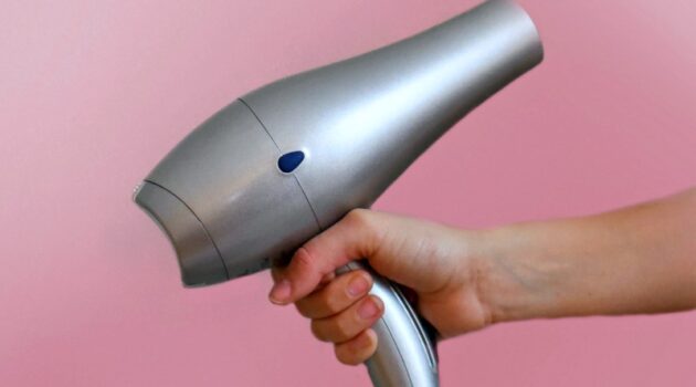 Silver hair dryer being held against a pink background