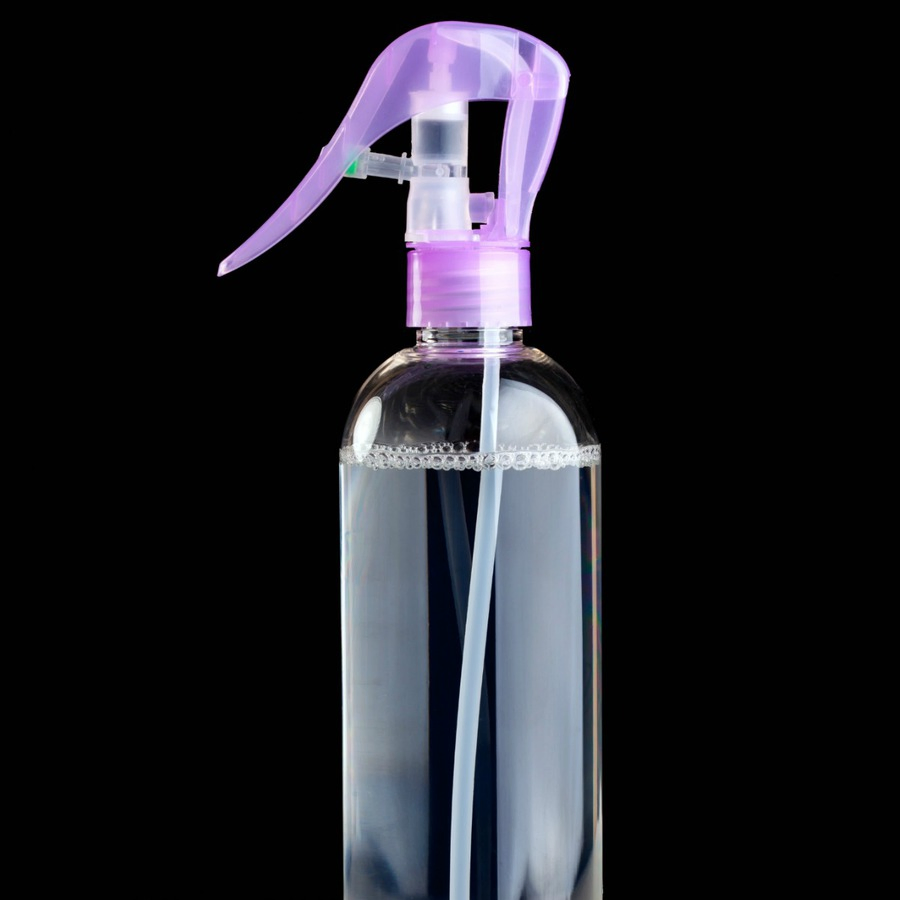 Close up of clear spray bottle with purple top filled with dry shampoo against a black background