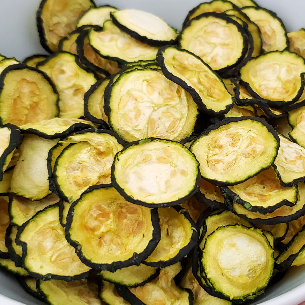 Close up of white bowl full of homemade zucchini chips on a blue painted wood table