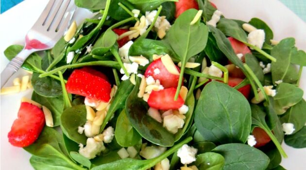 Close up of strawberry spinach salad on white plate with silver fork