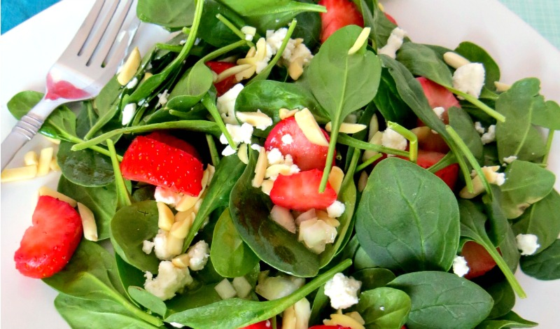Close up of strawberry spinach salad on white plate with silver fork