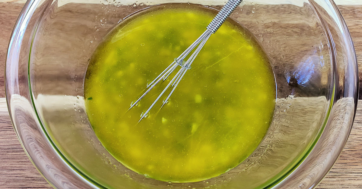 Rice vinegar, olive oil, sugar, garlic and jalapeno being whisked together in a glass mixing bowl.