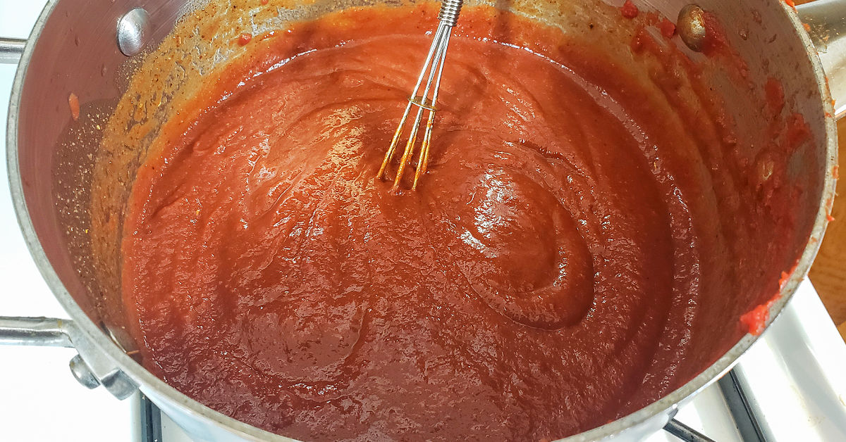 Tomato paste being whisked into chicken stock, spices and butter mixture.