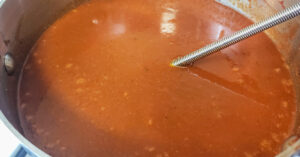 Remaining chicken stock being whisked into red sauce in pan.