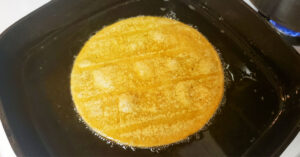 Corn tortilla being fried in cast iron skillet.