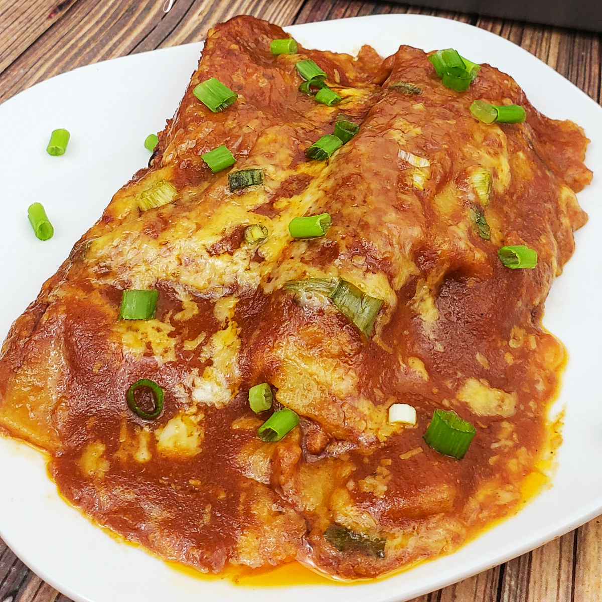 Two cheese chicken enchiladas on white plate and garnished with green onions.