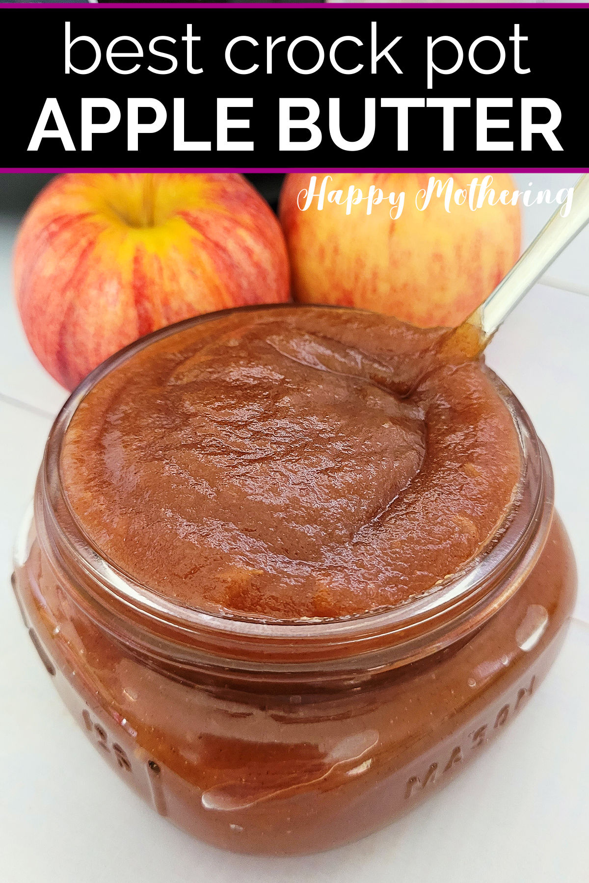 A spoon in a half pint jar of homemade apple butter with fresh apples in the background.