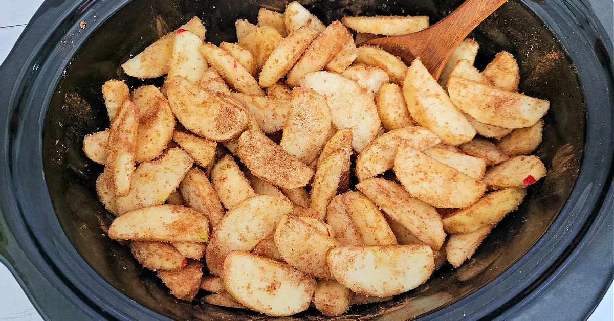 Apple slices coated in sugar and spices in crock pot.