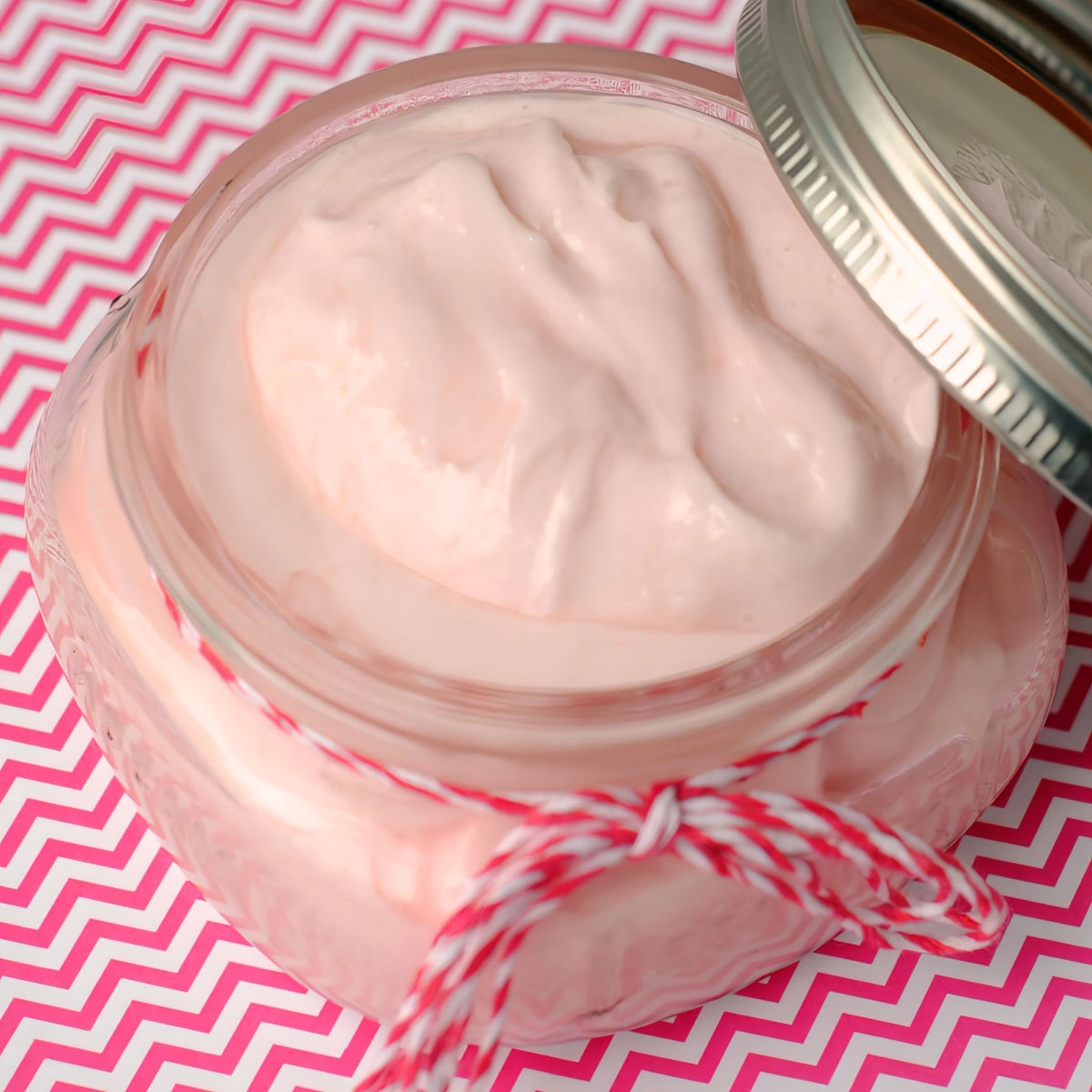 Close up of homemade peppermint body butter in a squat mason jar on chevron paper