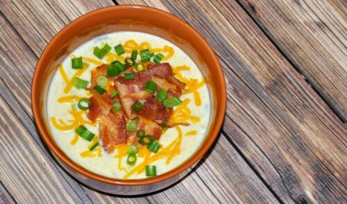 Delicious bowl of loaded leftover baked potato soup on a wood table
