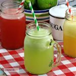Close up of glass jars with handles of watermelon, cucumber and orange agua fresca served with paper straws