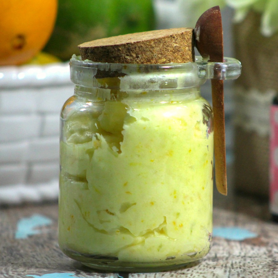 Close up of citrus body butter in glass jar with cork lid and wood spoon attached to the side of the jar