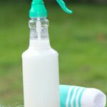 Spray bottle of window cleaner on bamboo cutting board with towel on grass