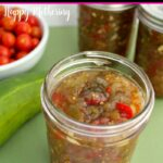 Open pint jar of homemade sweet pickle relish on green counter with cucumber, white bowl of cherry tomatoes and two sealed cans of relish.
