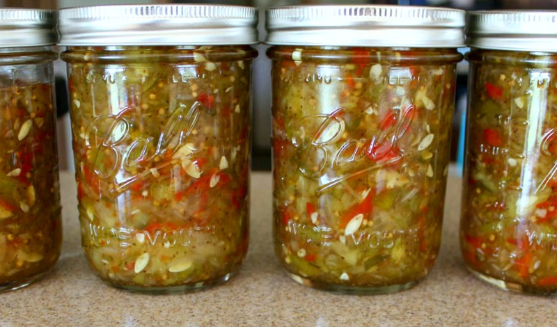 Four pint jars of homemade sweet pickle relish that has been canned, sitting on a counter.