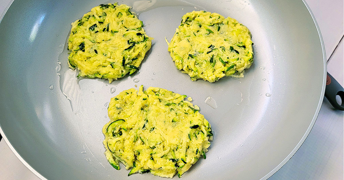 Raw zucchini fritters in a ceramic coated frying pan.