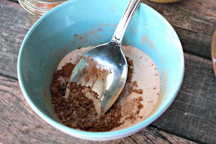 Blue bowl with cocoa powder and cornstarch in it that is being mixed with a silver spoon to make bronzer powder