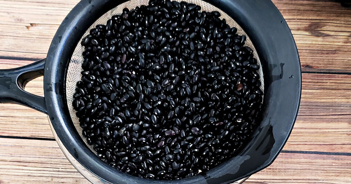 Black beans that have been sorted and rinsed in a strainer.