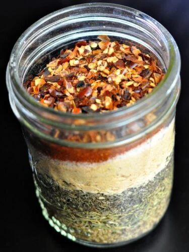 Italian seasoning ingredients layered in a mason jar on a dark background