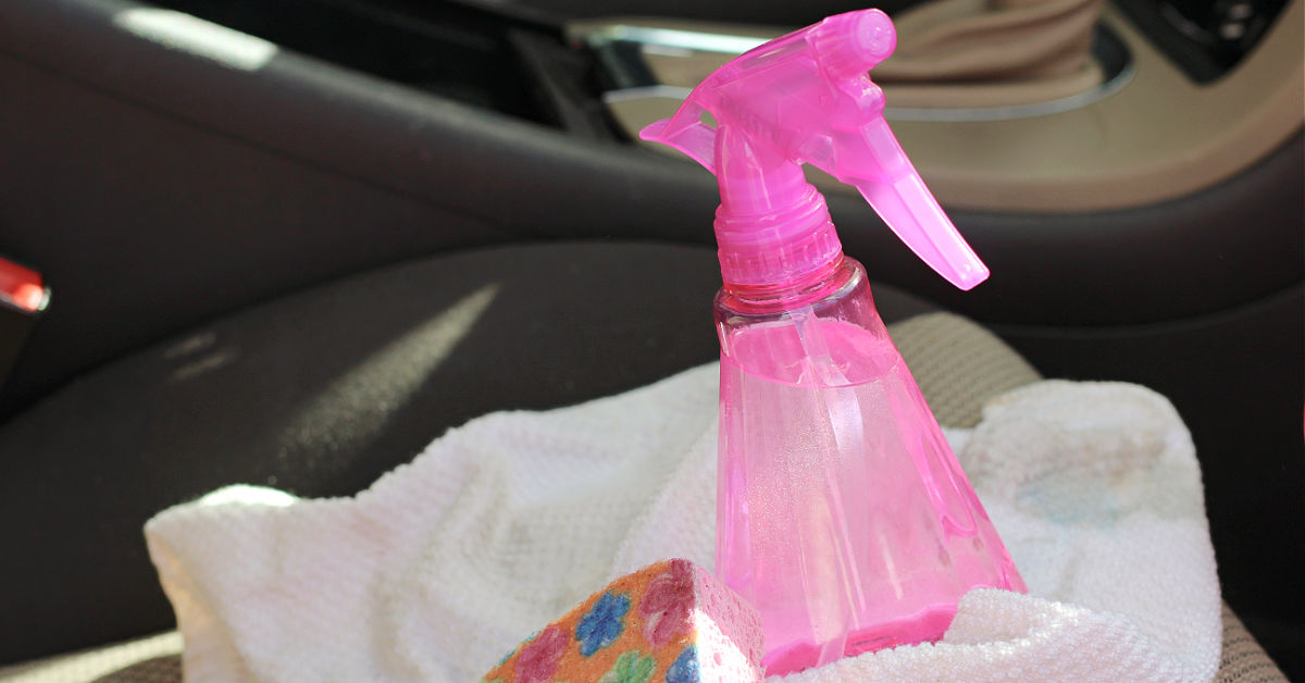 Pink spray bottle of homemade upholstery cleaner on car seat with sponge and towel.