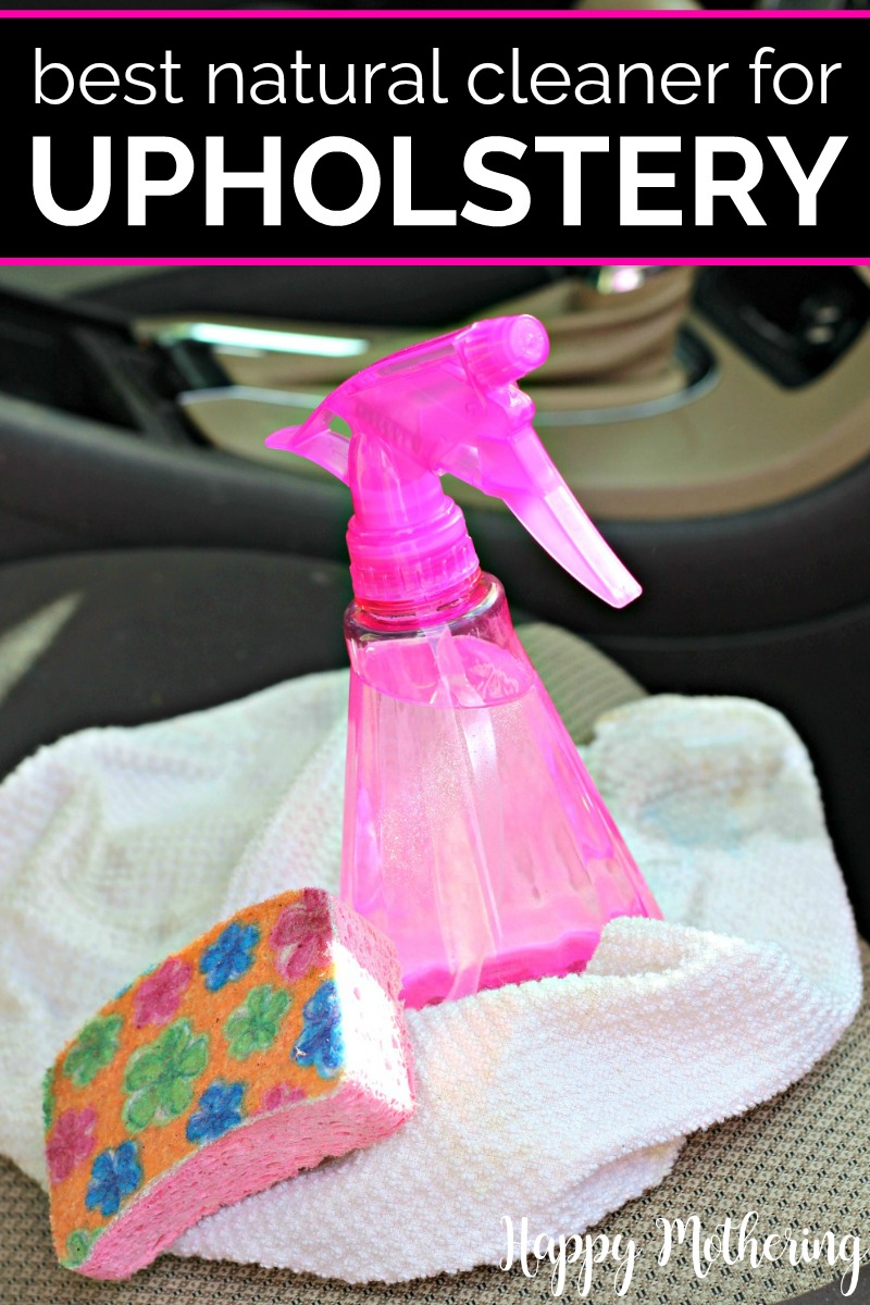 Plastic pink spray bottle filled with homemade upholstery cleaner sitting on a car seat with a pink sponge and white towel