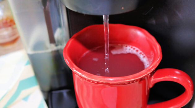 Red mug catching clean water after cleaning the Keurig coffee maker with vinegar.