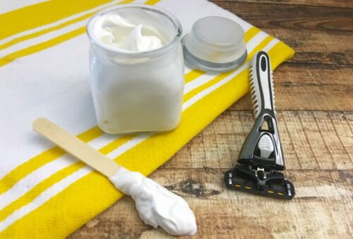 DIY shaving cream on a wood craft stick on a table next to a jar and a razor.