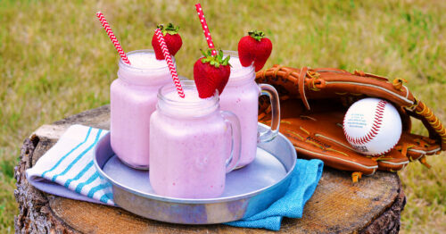 Three strawberry milkshakes on a tray outside next to a baseball mitt.