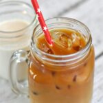 Mason jar with handle of cold brew coffee and sweet cream creamer with a red straw with white stars on a white background.