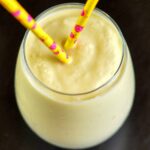 Close up of clear glass of Mango Pineapple Coconut Milk Smoothie with two yellow paper straws