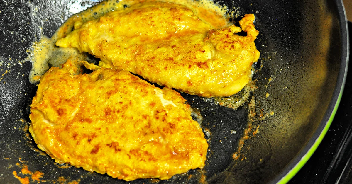 Dredged chicken breast cutlets being sautéed in a skillet.