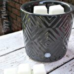 Black wax warmer on white wood table in front of brick wall