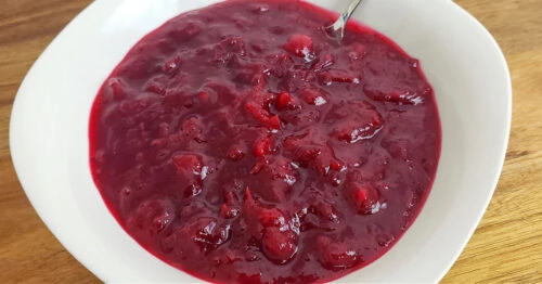 Homemade cranberry sauce in white serving bowl with spoon.