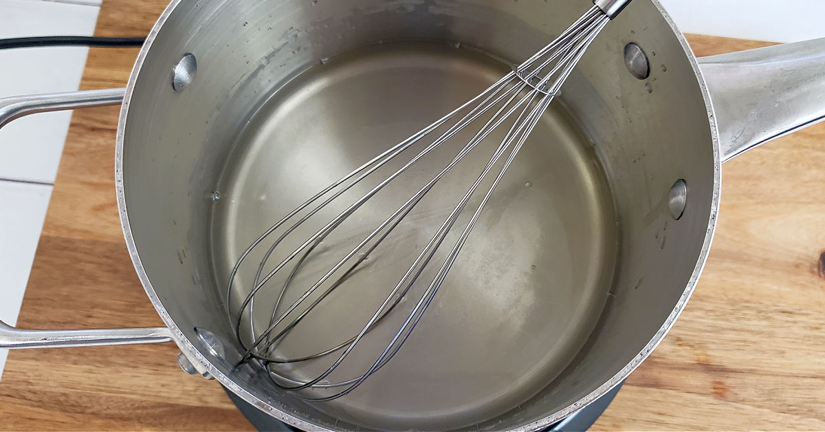 Sugar dissolved in water in saucepan with whisk.