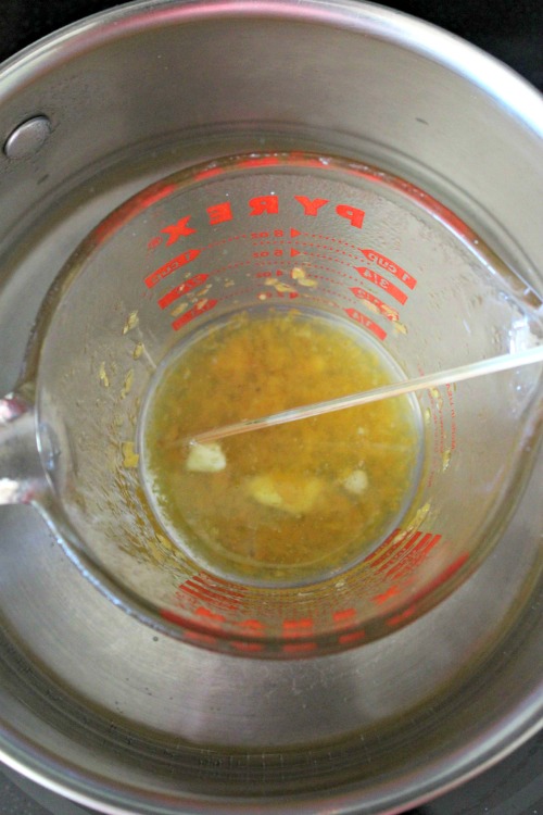 Ingredients for peppermint lip balm in glass measuring cup in pan of water