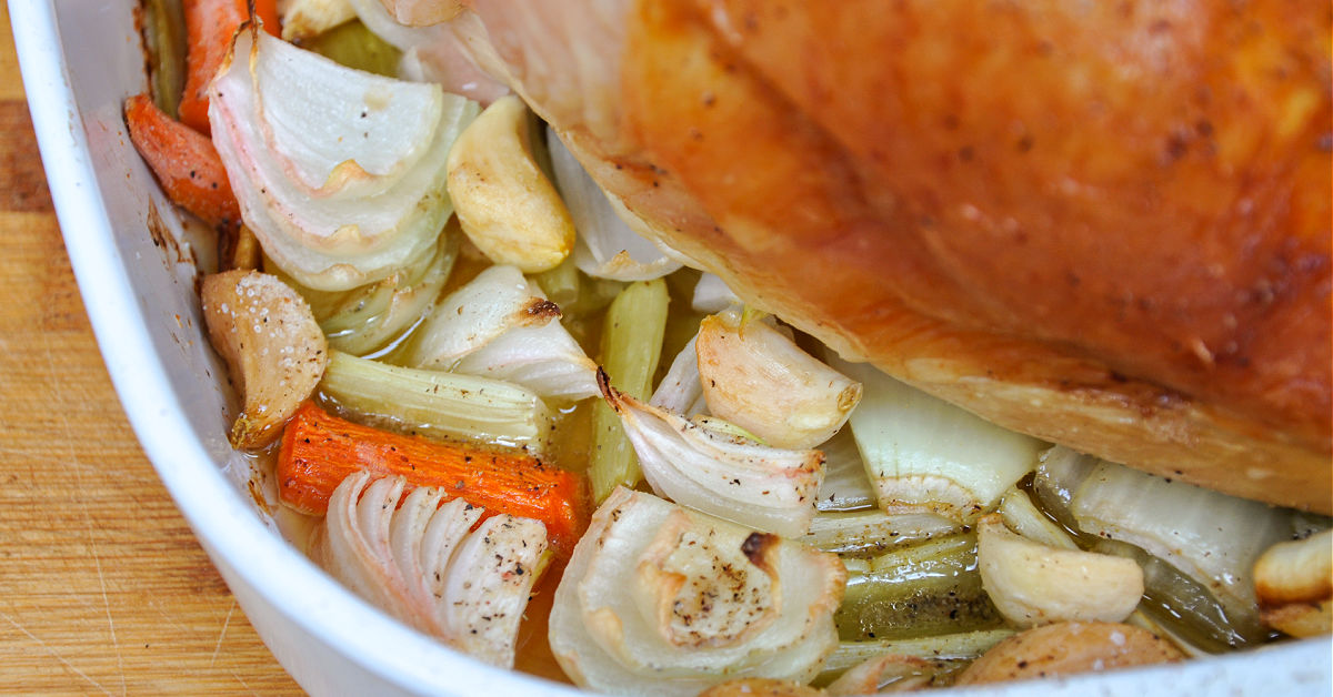 Close up of drippings with veggies from oven roasting turkey breast.