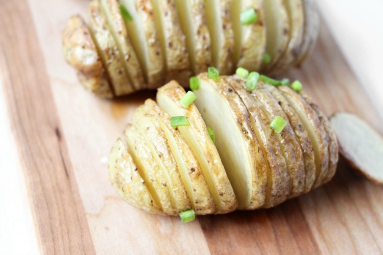 Baked Hasselback potatoes resting on a cutting board and topped with green onions