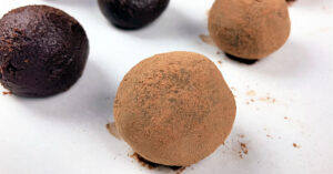 Chocolate truffles coated in cocoa powder on a parchment paper lined cookie sheet.